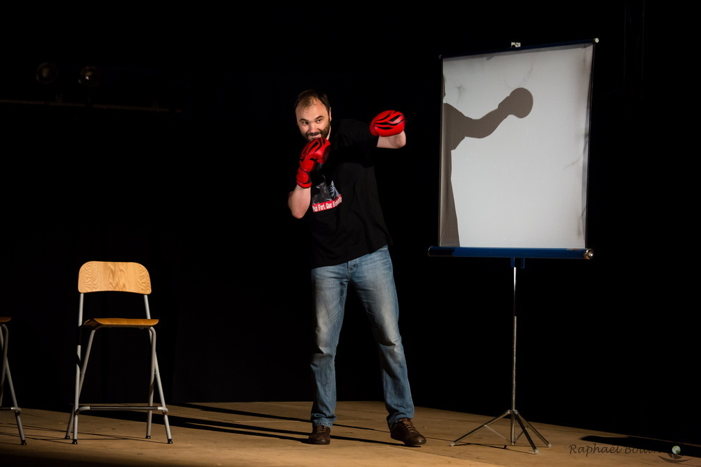 Un homme avec des gants de boxe au milieu d'une scène entre un tabouret et un pa
