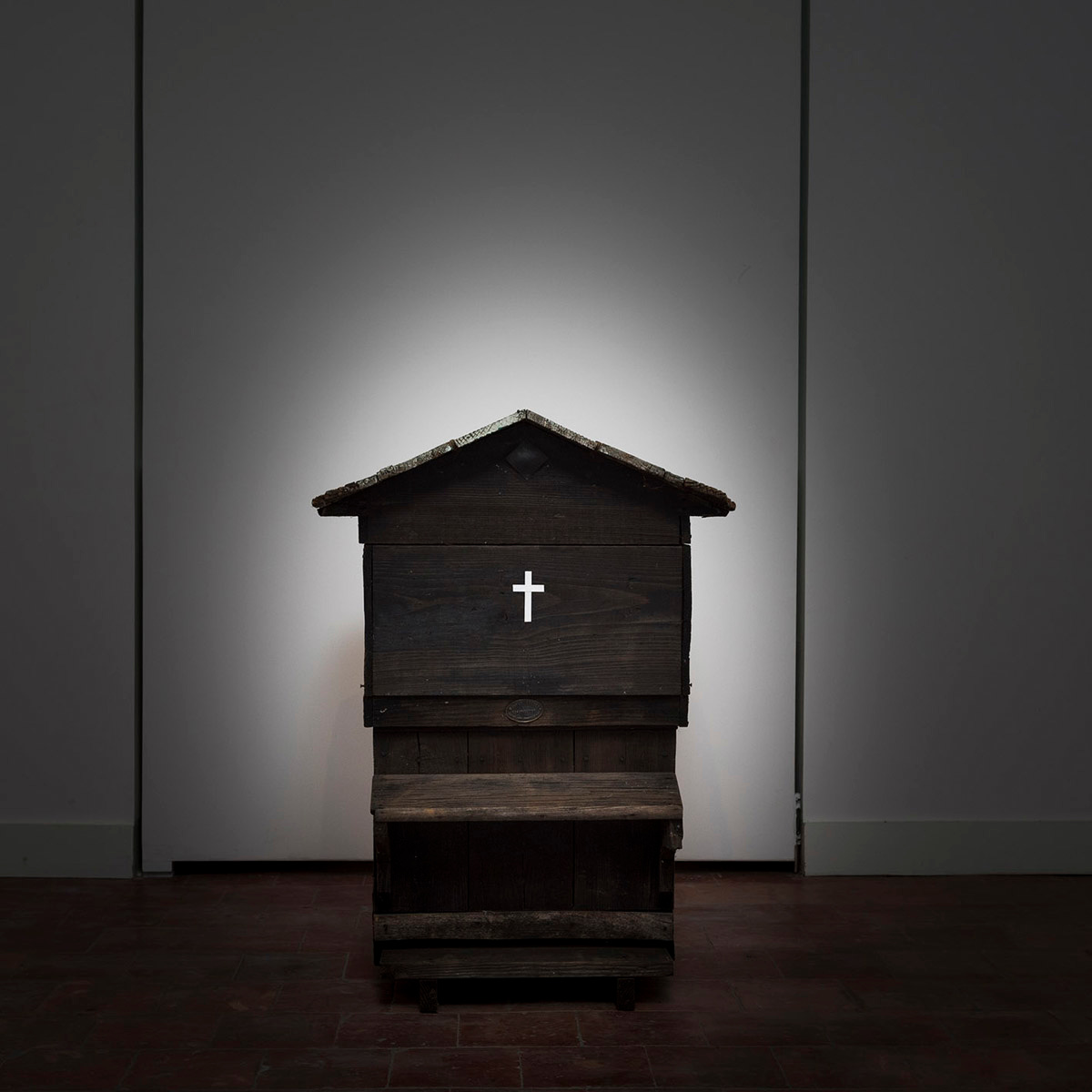 La photographie montre une ruche sombre ornée d'une croix blanche