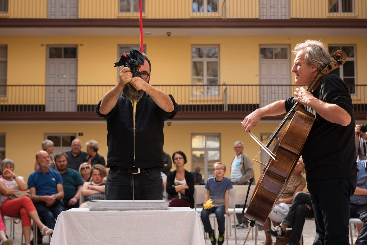 La photographie montre un violoncelliste et Olivier Darné pressant du miel