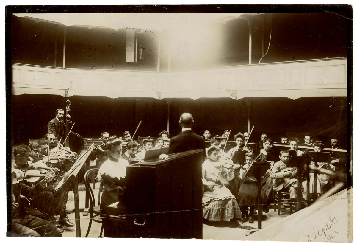 La photographie montre une répétition d'orchestre à l'intérieur du théâtre du Fa
